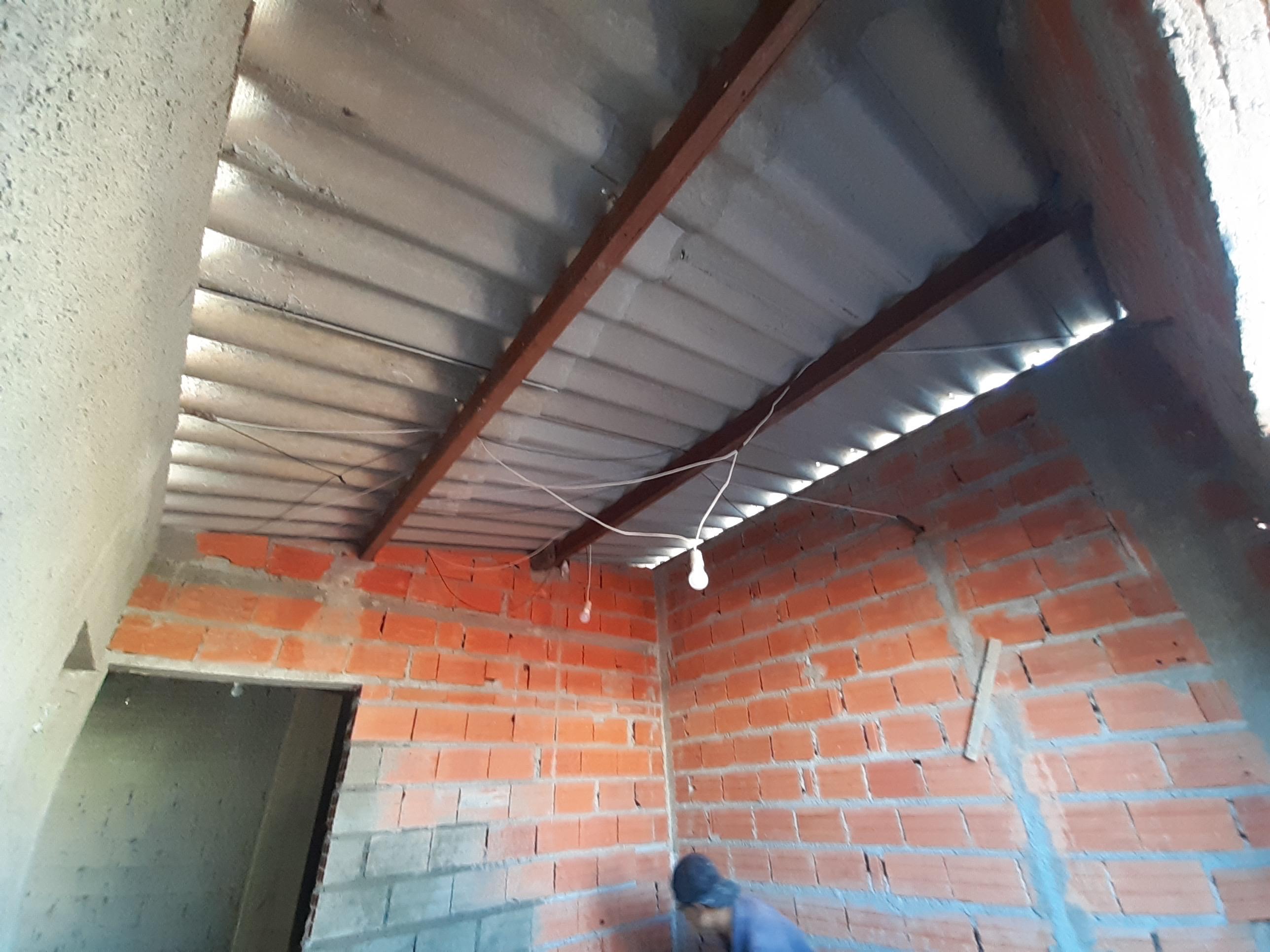 interior de construção com parede de tijolo vermelho, teto metálico com estruturas de ferro e uma lâmpada pendente, pessoa em azul na parte inferior
