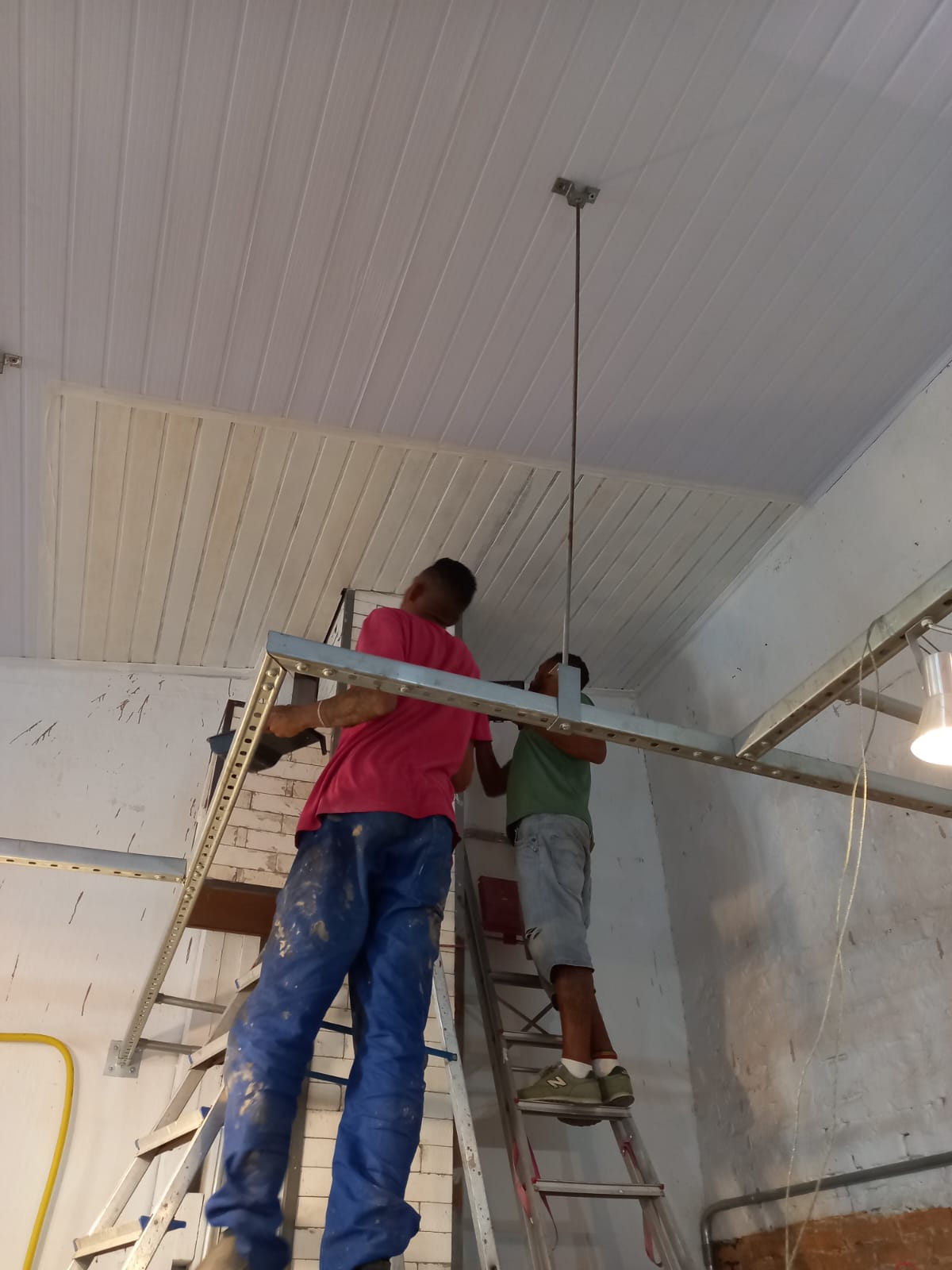 duas pessoas em escadas trabalhando em um teto com painéis de metal branco